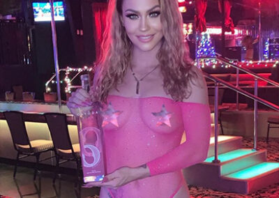 Girl at strip club holding bottle up for the camera